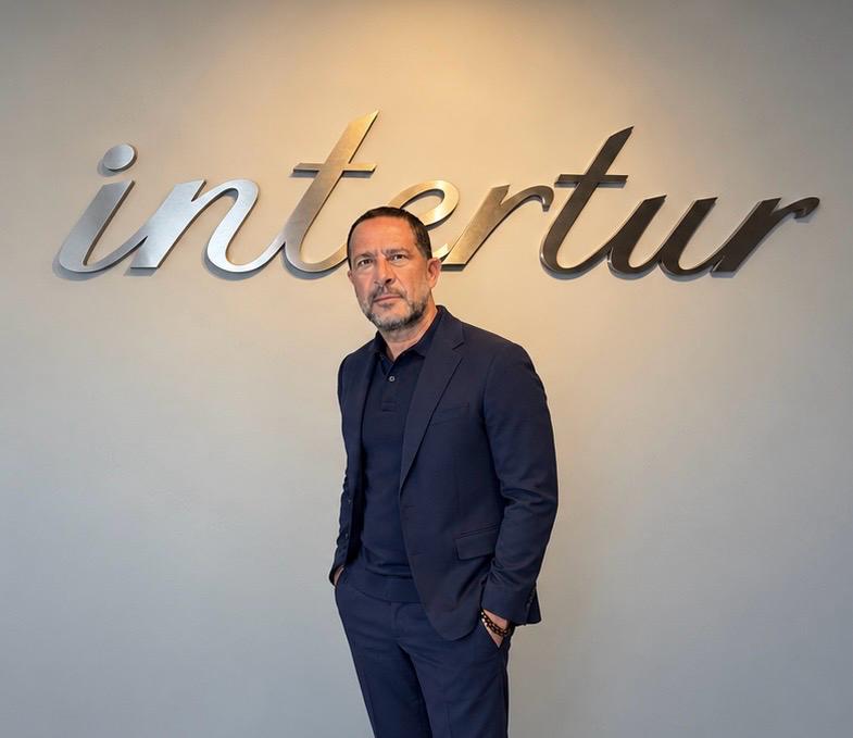 Retrato na sede da Intertur, diante do logotipo da agência.